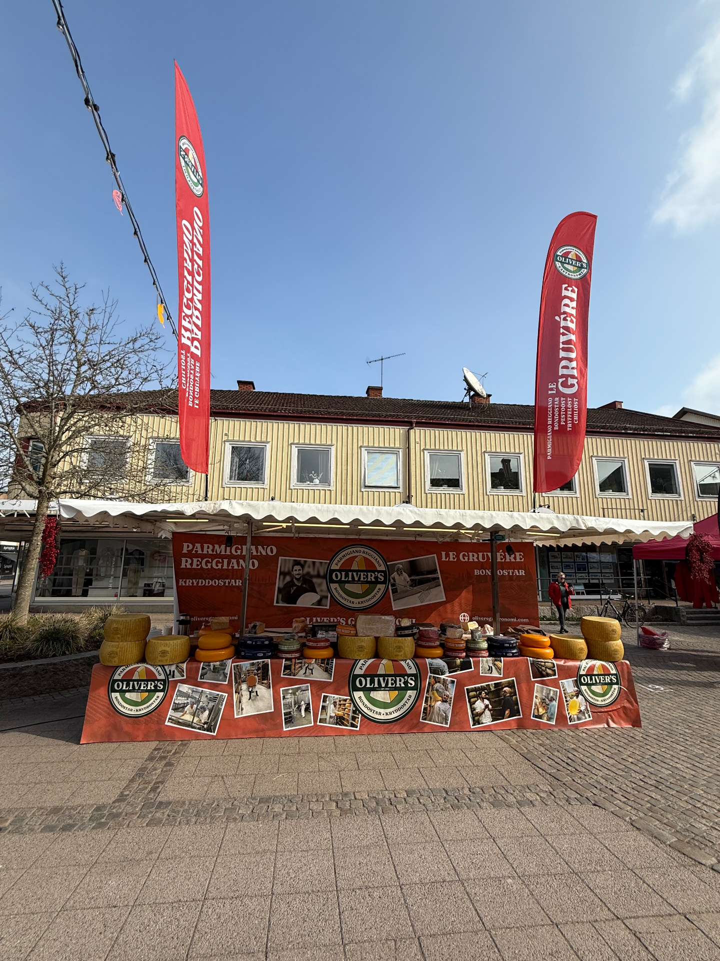 Oliver's Gastronomi-stånd på torgmarknad med osthjul och flaggor